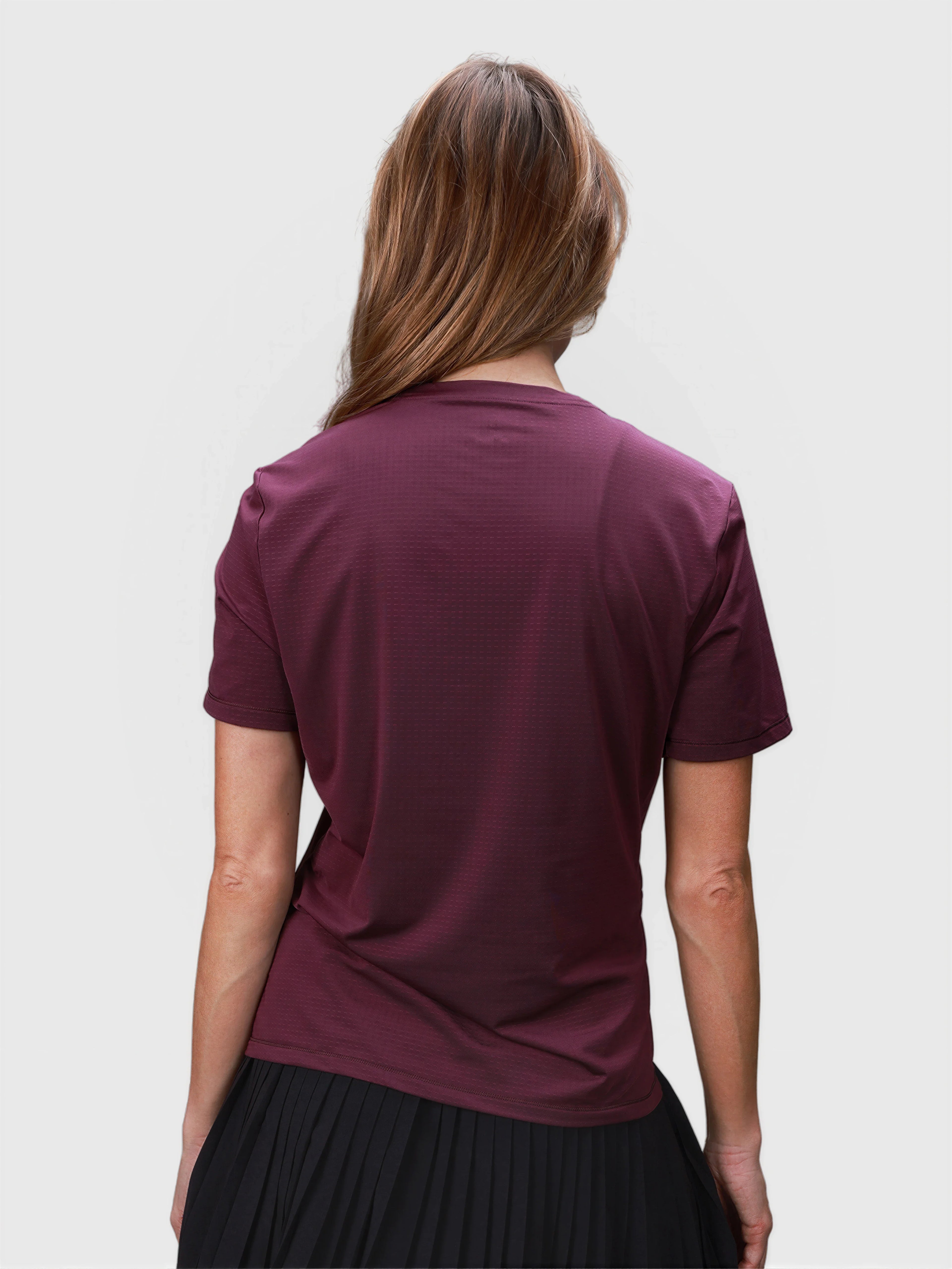 Woman seen from back wearing plum PowerMove Performance tee with short sleeves and black pleated skirt